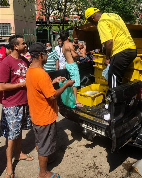 Equipe distribuindo peixe a moradores, direto da caçamba de uma caminhonete, em um condomínio.